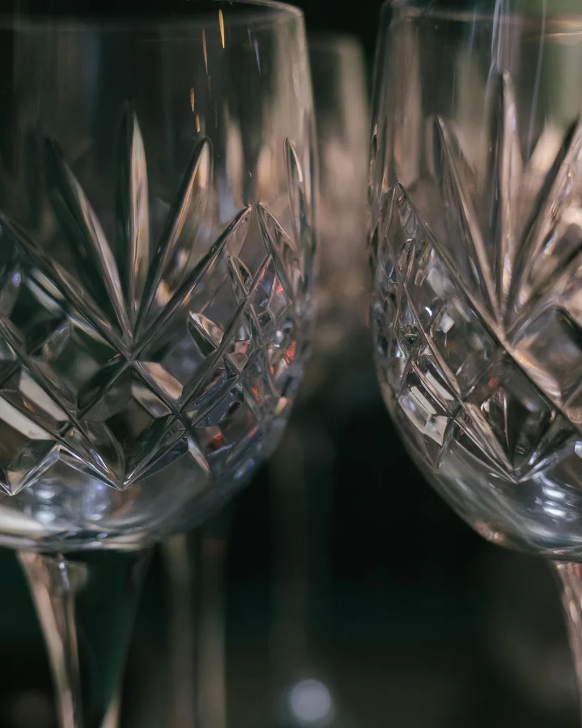 Detalle de dos copas de cristal talladas con motivos de rombos y abanicos, iluminadas de lado sobre fondo oscuro.